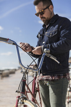 Hip man buttoning his shirt next to vintage bicycle