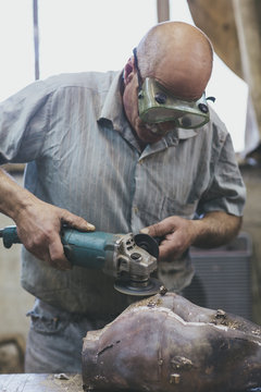 Old craftsman sanding a bronze sculpture