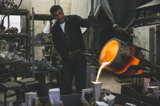 Middle aged man pouring melted bronze into molds using a crucibl