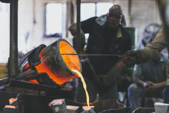 Closeup of hands racking melted bronze into molds using a crucib
