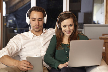 Paar beim Websurfen und Musik hören mit Tablet und Laptop