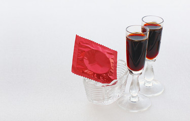 Red condom in a small vase and two glasses with a dark drink