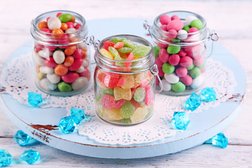 Multicolor candies in glass jars on color wooden background