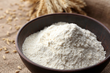 Flour in bowl with ears and grains on sackcloth background