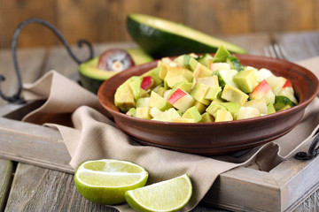 Salad with apple and avocado in bowl on tray on table close up