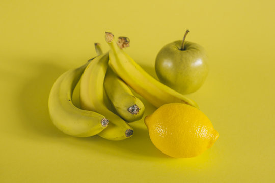 bananas apple and lemon on yellow background