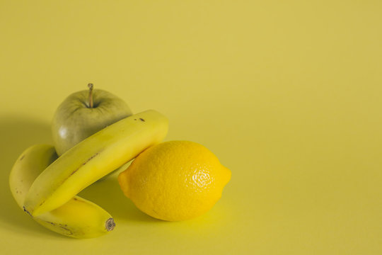 bananas apple and lemon on yellow background