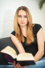 Obraz premium Mädchen mit Buch sitzt Zuhause auf dem Sofa