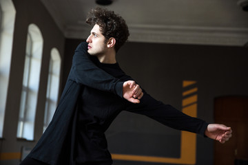 Handsome young male dancer stretching at gym