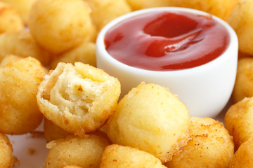 Bowl of fried small potato balls on white. Pot of ketchup.