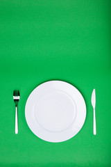 white plate, fork and knife on green background