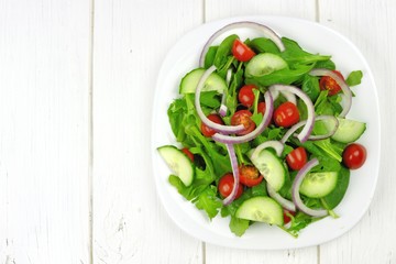 Mixed green salad on white wood, overhead view