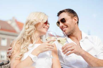 smiling couple in sunglasses drinking wine in cafe