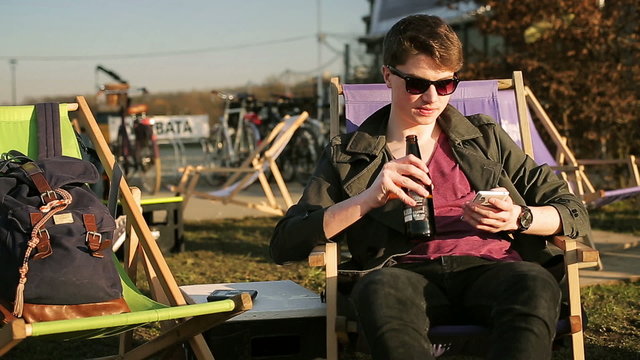 Student drinking beer on sunbed and smiling to the camera