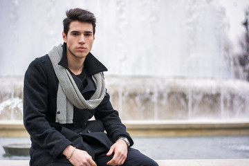 Obraz premium Stylish trendy young man sitting outdoor at big fountain