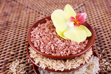 Different types of rice in bowls on wicker background