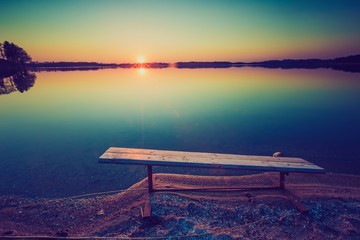 Vintage photo of bench on lake shore at sunset