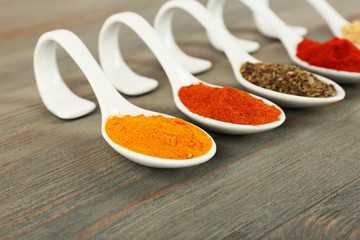Different kinds of spices in spoons on wooden background
