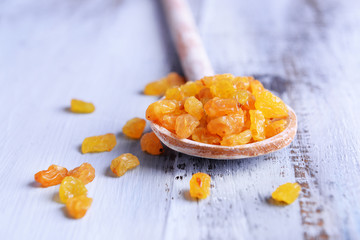 Raisins in spoon on color wooden table background