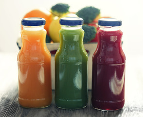 Bottles of juice with fruits and vegetables on table close up