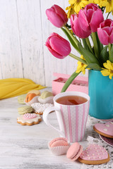 Composition of spring flowers, tea and cookies on table