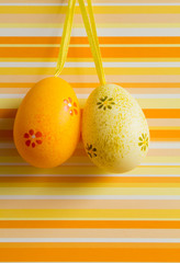 Orange and yellow hanged Easter eggs on striped background