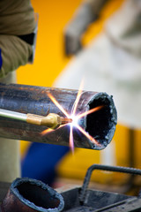 Acercamiento de un trabajador llevando a cabo el corte de un tubo metálico utilizando un equipo de soldadura