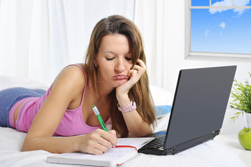 bored college student girl lying on bed with computer studying