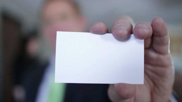 Business man holds up a blank business card to the camera.  If last frame is frozen, various text or graphics can be added to the card.  Camera mounted on moving jib arm.