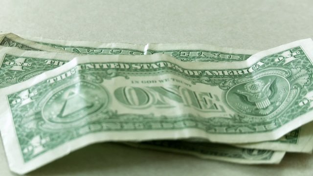 Hand puts one dollar bills and then a couple of five dollar bills down on to a rough stack.