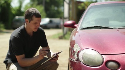 Insurance person inspects the damage on a car and makes notes on a digital tablet.