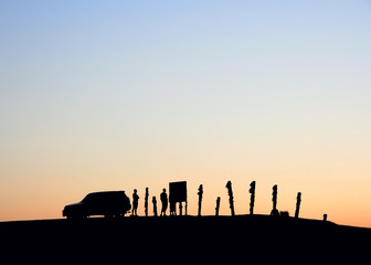Silhouettes of a car and people on the sky background