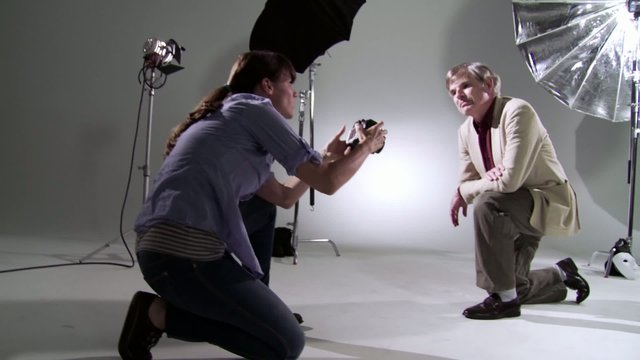 Attractive young woman taking photographs with actor/model studio.  Both kneeling on studio floor.