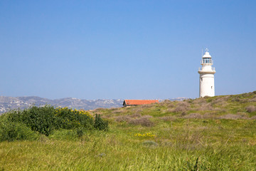Fototapeta na wymiar Green meadow, lighthouse, roof of the house and mountains in the