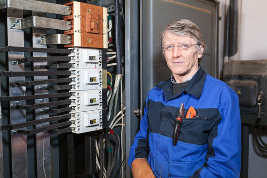 Mature electrician worker stands at work place and looking