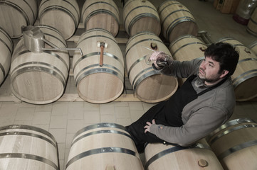 Winemaker tasting wine amongst oak casks.