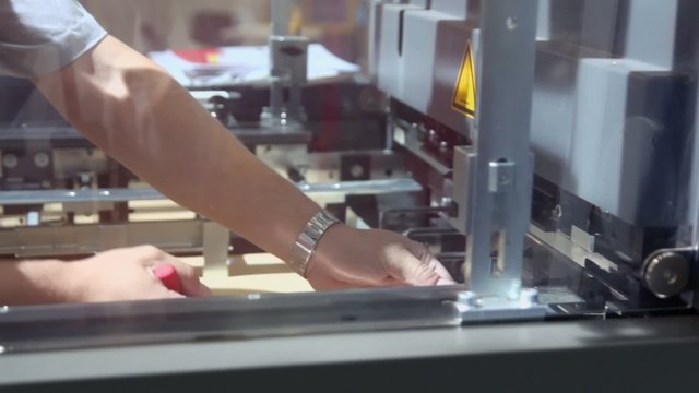 Man screws nut in mechanism of printing machine in conveyer