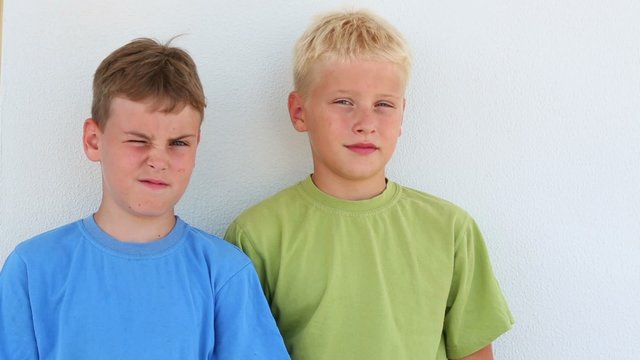Two boys in colored T-shirt squint near the white wall