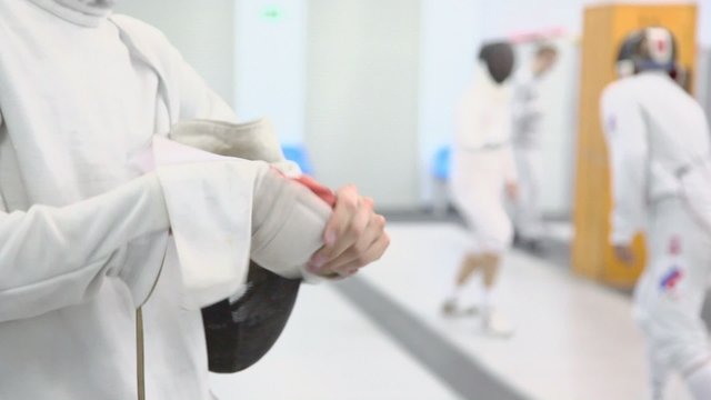 Fencer with rapier puts off glove during training in gym, closeup view