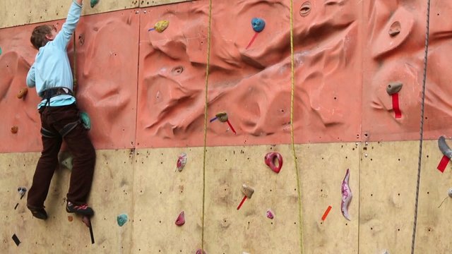 Boy cross relief part of vertical wall at rock-climbing gym hall