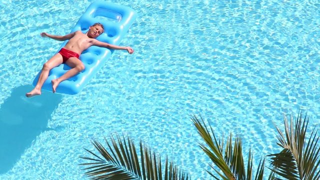 Boy lies with arms stretched to sides on inflatable mattress