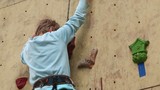 Close-up boy-beginner tries to climb up at rock-climbing wall