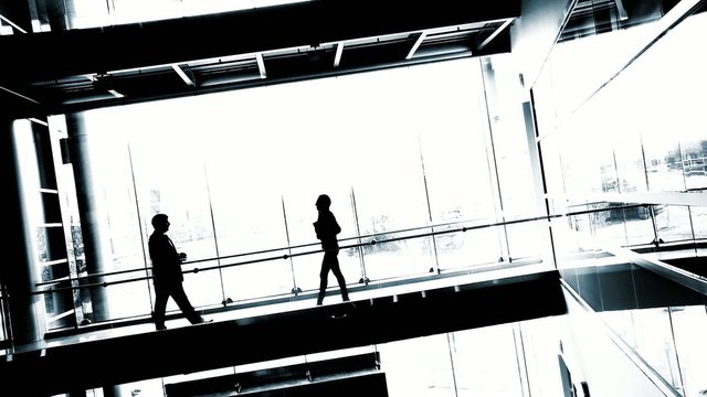 Silhouetted businessman and woman meet against a backdrop of white windows.  High contrast clip, wide view with canted camera.