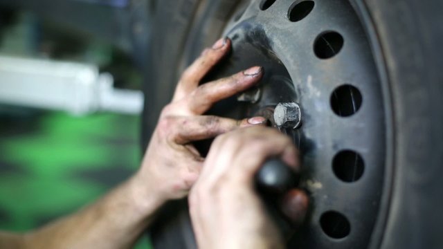 Male hands mount forelock on nut of car wheel at service station