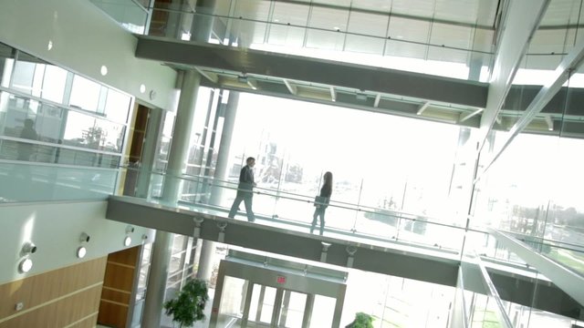 Backlit businessman and woman meet against a backdrop of white windows.  Low contrast clip, wide view with canted camera.