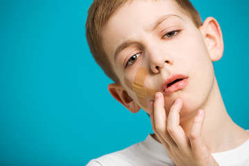 Close up portrait of unhappy boy with adhesive plaster on his ch