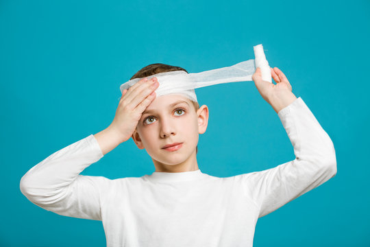 Portrait of unhappy boy in white clothes taping up bandage on hi