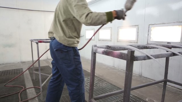 Man in protective clothes works in paint-spraying booth