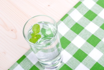 glass of clean water with mint on a table covered with a checker