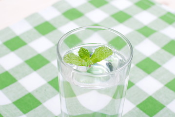 glass of clean water with mint on a table covered with a checker